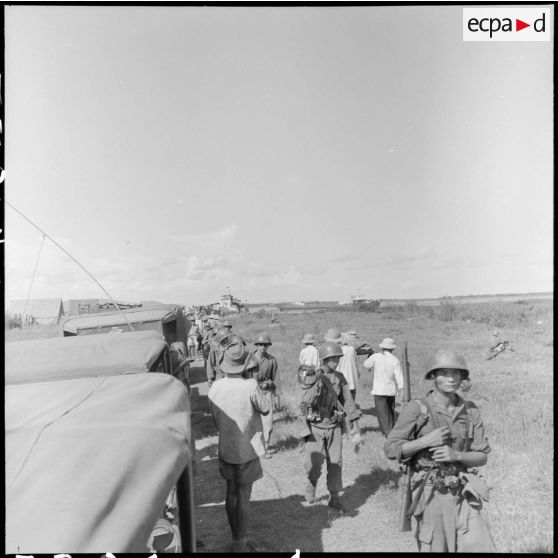 Une colonne de soldats venant de débarquer d'un LCT croise des brancardiers transportant les morts et les blessés d'un récent engagement, au cours de l'opération Claude.