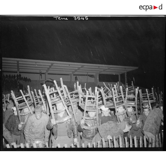 Les spectateurs se protègent de la pluie pendant le combat de boxe.