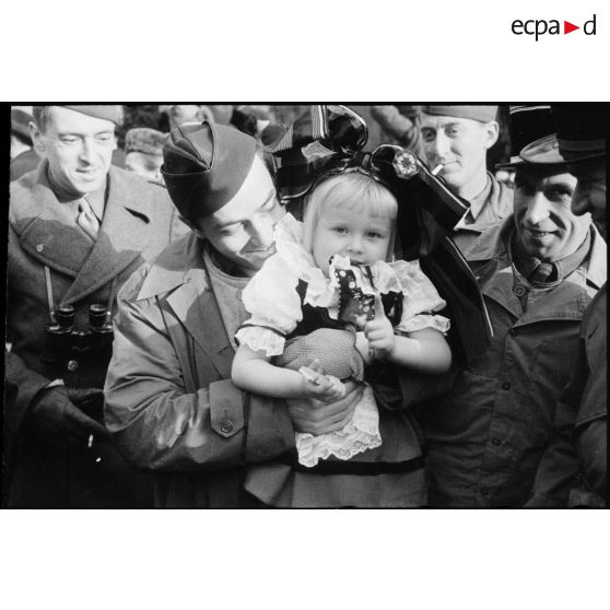 Pierre Bourdan porte une enfant revêtue du costume traditionnel alsacien dans la commune de Erstein (Bas-Rhin) libérée.